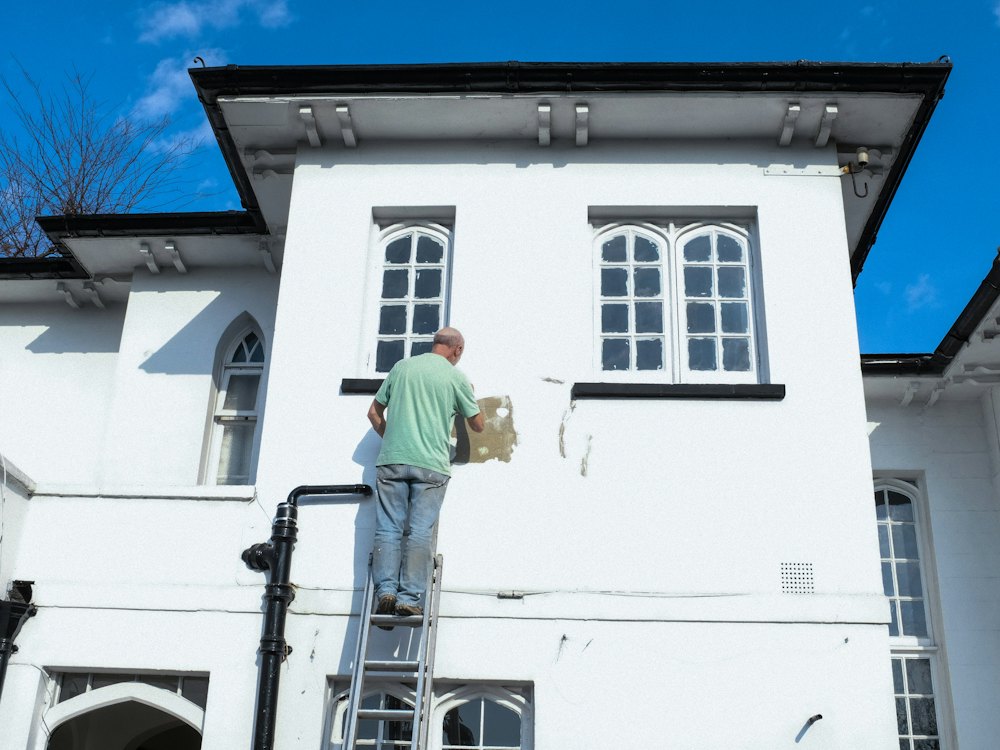 Peintre sur échelle repeignant la façade blanche d'une maison